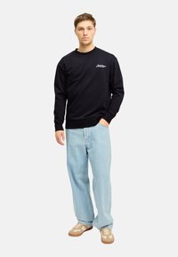 Sudadera negra con cuello redondo, puños y dobladillo de canalé, combinada con pantalones vaqueros de pierna ancha en azul claro y zapatillas beige.
