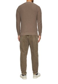Beiger Strickpullover mit strukturiertem Muster, rundem Halsausschnitt und gerippten Bündchen. Kombiniert mit olivfarbenen Cordhosen und weißen Sneakers.