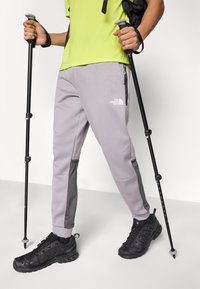 Γκρι παντελόνια πεζοπορίας με υφασμάτινες πλαϊνές πινελιές, με το λογότυπο του North Face. Συνδυασμένα με μαύρα αθλητικά παπούτσια και μπαστούνια πεζοπορίας.