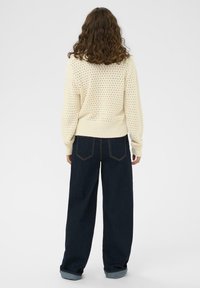 Pull en maille ivoire avec un motif texturé, des poignets et une taille côtelés. Associé à un jean en denim sombre ample, retroussé aux poignets.