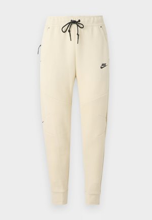 Pantaloni de trening Nike în bej deschis, cu un logo negru, talie cu șnur, mansete elastice și două buzunare laterale cu accente texturate.