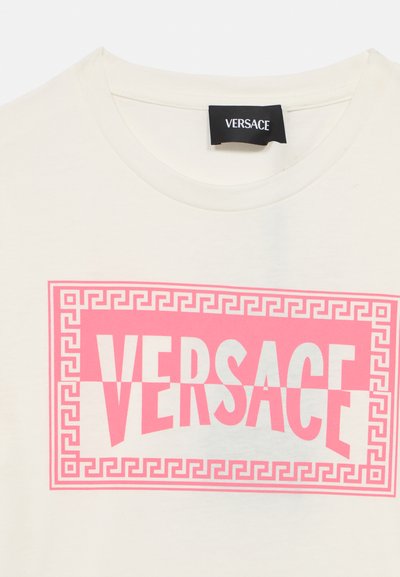 Világosbézs pamut póló merész rózsaszín "VERSACE" felirattal, geometrikus keretes mintával. Kerek nyakú, rövid ujjú.