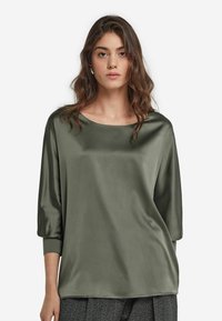Olivgrön satintröja med rund halsringning, trekvartslånga ärmar och en slät, glänsande textur. Enkel, avslappnad design.