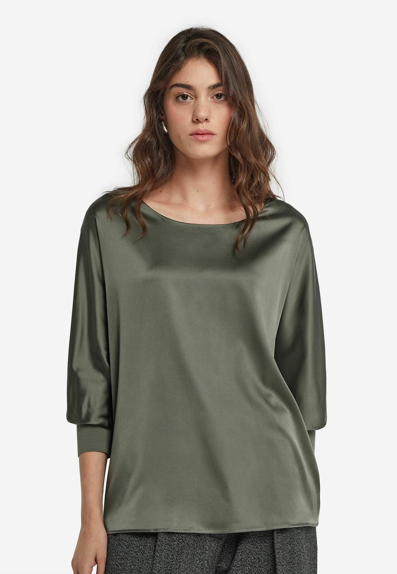 Olivgrön satintröja med rund halsringning, trekvartslånga ärmar och en slät, glänsande textur. Enkel, avslappnad design.