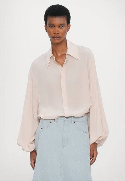 Blusa de manga larga color rosa claro con cuello tipo camisa y cierre delantero de botones. Presenta mangas voluminosas y una tela suave y fluida.