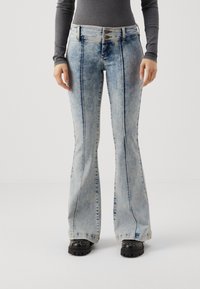 Jean évasé bleu clair avec un effet délavé, des détails de couture le long des coutures, et une fermeture à trois boutons à la taille haute.