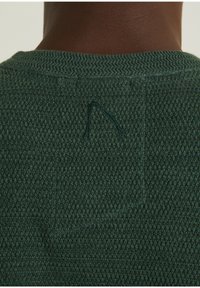 Strukturierter grüner Strickpullover mit Rundhalsausschnitt. Verfügt über ein kleines gesticktes Detail nahe der oberen Rückseite. Kreisform am Halsausschnitt.