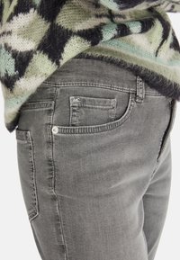 Grijze denim jeans met een getailleerde pasvorm, voor- en achterzakken, en een subtiele vervaagde textuur. Label zichtbaar nabij de tailleband.