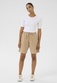 Beige lehké šortky s elastickým pasem a šňůrkou, které mají dvě přední kapsy. Spárováno s přiléhavým bílým tričkem s krátkým rukávem.