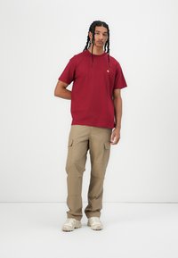 Maroon short-sleeve t-shirt with a small logo, paired with light brown cargo pants featuring multiple pockets and a relaxed fit.