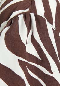 Tecido com padrão de zebra em castanho e branco, apresentando um acabamento texturizado e detalhes franzidos, exibindo linhas fluidas e contraste de cores.