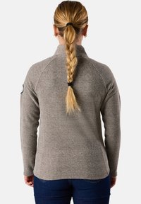 Pullover texture marrone chiaro con colletto alto e maniche lunghe, con cuciture raglan e un patch circolare sulla spalla sinistra.