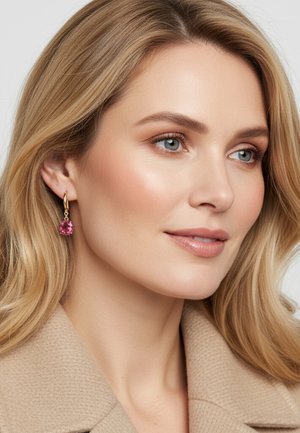 Gouden creolen met een ronde roze edelsteen als hanger. Het model heeft blond haar en een gladde, natuurlijke huidtextuur.