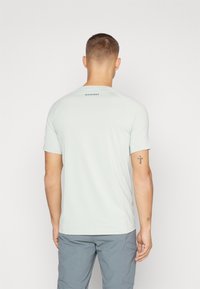 Lys grå kortermet skjorte med rund hals, jevn tekstur, og "Mammut"-logo på ryggen, brukt sammen med grå shorts.