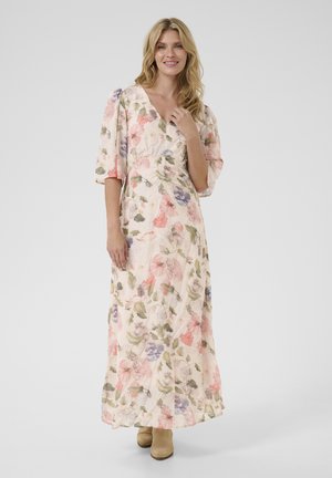 Rochie maxi florală din material piersiciu deschis, cu modele în tonuri de roz, violet și verde. Are decolteu în V și mâneci ample. Asortată cu cizme de gleznă bej.