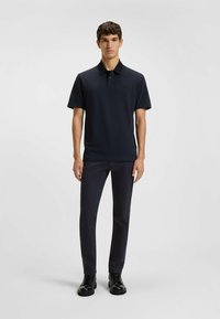 Camiseta polo azul marino con cuello y mangas cortas, con un logotipo discreto. Se lleva con pantalones oscuros y botas negras de cordones.