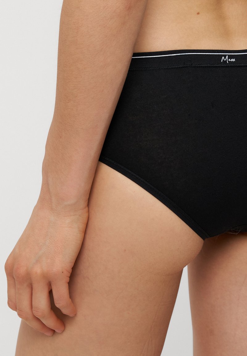 Schwarze Baumwollslips mit glatter Textur, ausgestattet mit einem kontrastierenden weißen Bund und minimalistischem Design. Sichtbare Hand, die auf dem Oberschenkel ruht.