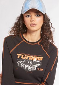 Maglietta nera a maniche lunghe con cuciture arancioni, caratterizzata da una stampa grafica di auto elaborate e dalla parola "Tuning". Cappellino grigio con design di fiamme blu.