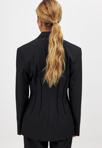 Black tailored blazer featuring a structured design, sharp shoulder lines, and contoured seams. Smooth fabric and elegant silhouette.