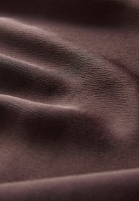 Měkká hnědá látka s jemným, texturovaným povrchem a jemnými záhyby vytvářejícími variace světla a stínu.