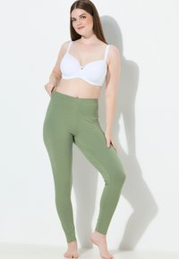 Zielone legginsy wykonane z miękkiego, elastycznego materiału o gładkiej fakturze i elastycznym pasie, zestawione z białym biustonoszem.