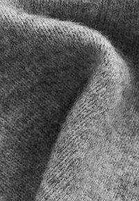 Grått stickat tyg med en mjuk textur, som har en lös väv, subtil fluffighet och en böjd draping som framhäver tjockleken.