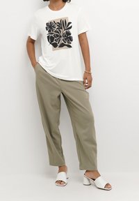 Camiseta blanca con estampado floral negro, combinada con pantalones khaki holgados y tacones abiertos blancos. Textura suave y ajuste relajado.