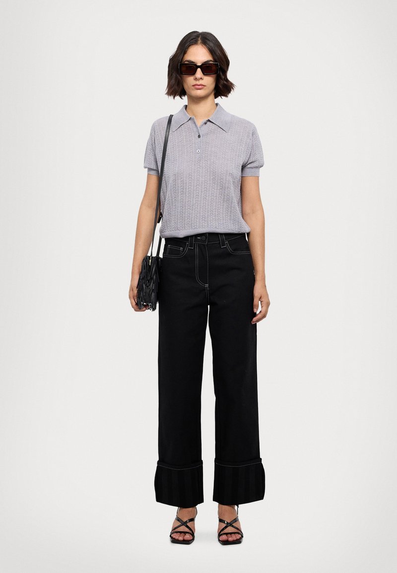 Polo shirt a maglia grigio chiaro con maniche corte, pantaloni neri a gamba larga con orlo a strisce svasato, sandali neri con bretelle e una piccola borsa nera.