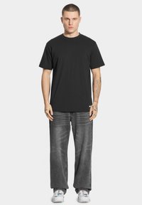 Czarny bawełniany t-shirt z klasycznym okrągłym dekoltem, w połączeniu z luźnymi, wyblakłymi szarymi dżinsami. Białe sneakersy dopełniają stylizację.