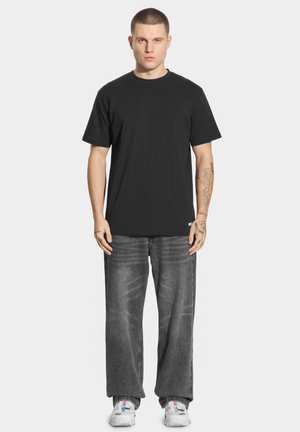 Czarny bawełniany t-shirt z klasycznym okrągłym dekoltem, w połączeniu z luźnymi, wyblakłymi szarymi dżinsami. Białe sneakersy dopełniają stylizację.