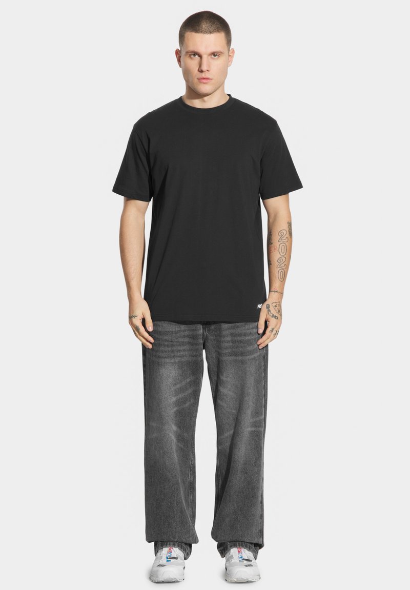 Czarny bawełniany t-shirt z klasycznym okrągłym dekoltem, w połączeniu z luźnymi, wyblakłymi szarymi dżinsami. Białe sneakersy dopełniają stylizację.