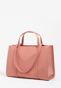 Miękka różowa torba na ramię z podwójnymi uchwytami i długim paskiem na ramię, o prostokątnym kształcie, gładkiej teksturze i obszytych krawędziach na białym tle.