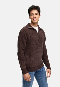Brun, ribbet strikpullover med lynlås krave, der har lange ærmer og en afslappet pasform, parret med blå jeans.