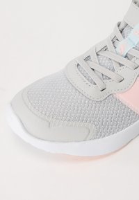 Chaussure de sport grise avec une tige en maille, semelle en caoutchouc et accents roses. Comprend des panneaux texturés et des lacets plats.