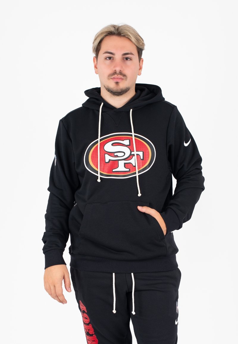 Zwarte hoodie met een opvallend rood-wit SF-logo, trekkoorden en een voorvak. Draagt bijpassende zwarte joggingbroek met rode tekst.