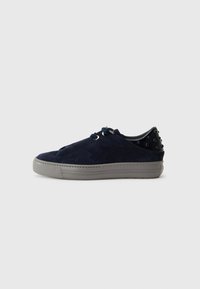 Baskets en suède bleu marine à lacets avec une semelle extérieure texturée grise et des clous noirs décoratifs sur le talon, présentant un design épuré et moderne.