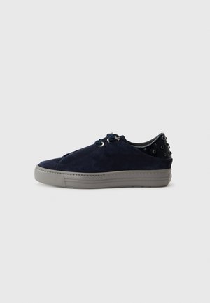 Baskets en suède bleu marine à lacets avec une semelle extérieure texturée grise et des clous noirs décoratifs sur le talon, présentant un design épuré et moderne.