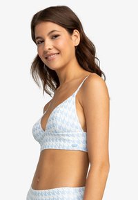 Sujetador bralette azul claro con patrón de houndstooth blanco, tejido suave, copas triangulares, tirantes ajustables y un pequeño logo en el lateral.