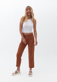 Top cropped bianco leggero abbinato a pantaloni cargo color ruggine con tasche laterali e una vestibilità rilassata. Sandali bianchi minimalisti.