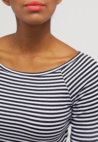 Svart och vit randig långärmad topp med vid halsringning och texturerad tyg. Närbild på halsringning och axlar.