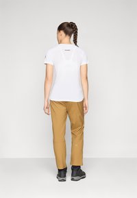 Λευκό αθλητικό T-shirt με κοντά μανίκια, εφαρμοστή σχεδίαση, υφασμάτινη πίσω πάνελ, σε συνδυασμό με καφέ παντελόνια πεζοπορίας και σκούρα παπούτσια.