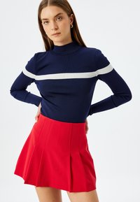 Maglia a maniche lunghe a righe navy con striscia orizzontale bianca, abbinata a una mini gonna rossa plissettata con vita aderente.