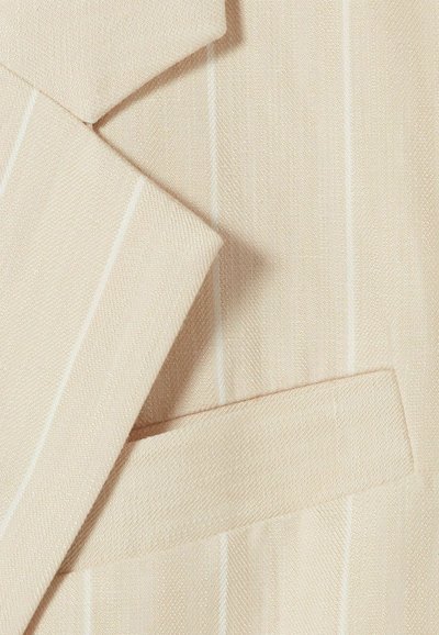 Tessuto beige chiaro con una trama sottile, caratterizzato da sottili righe bianche. Elementi includono un colletto piegato e un dettaglio con tasca.