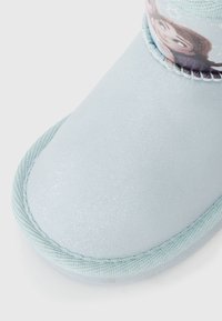 Stivaletto azzurro chiaro con una superficie liscia e lucida, bordo elastico con una stampa di personaggi e un bordo testurizzato per un tocco di dettaglio in più.