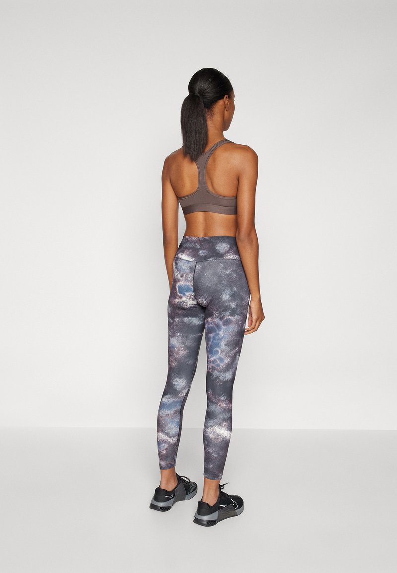 Soutien-gorge de sport marron avec un design dos nageur, associé à un legging taille haute avec un motif tie-dye multicolore. Chaussures de sport noires.