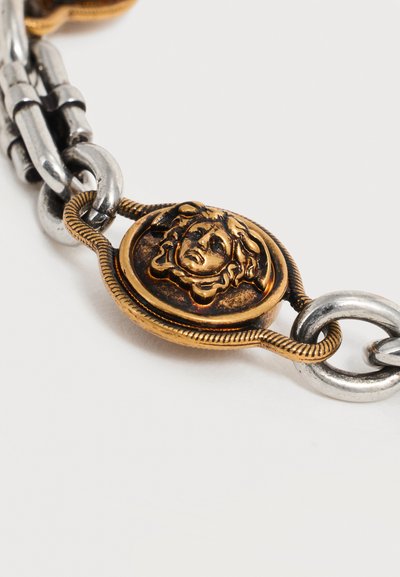 Κοντινό πλάνο αλυσίδας από χρυσό και ασήμι με κεντρικό μοτίβο το κεφάλι της Μέδουσας από χρυσό σε λευκό φόντο.