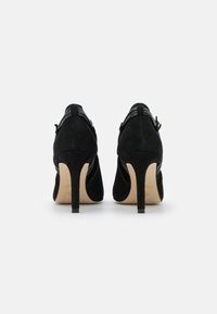 Mustat mokkanahka korkeakorkoiset kengät, joissa on leikattu muotoilu, sileä pinta, kapea korko ja vaakasuorat nahkaakcentit takana.