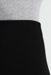 Pletený top s texturovanou šedou horní částí a černou žebrovanou spodní částí, zdůrazňující dvoubarevný design a kontrastní materiály.