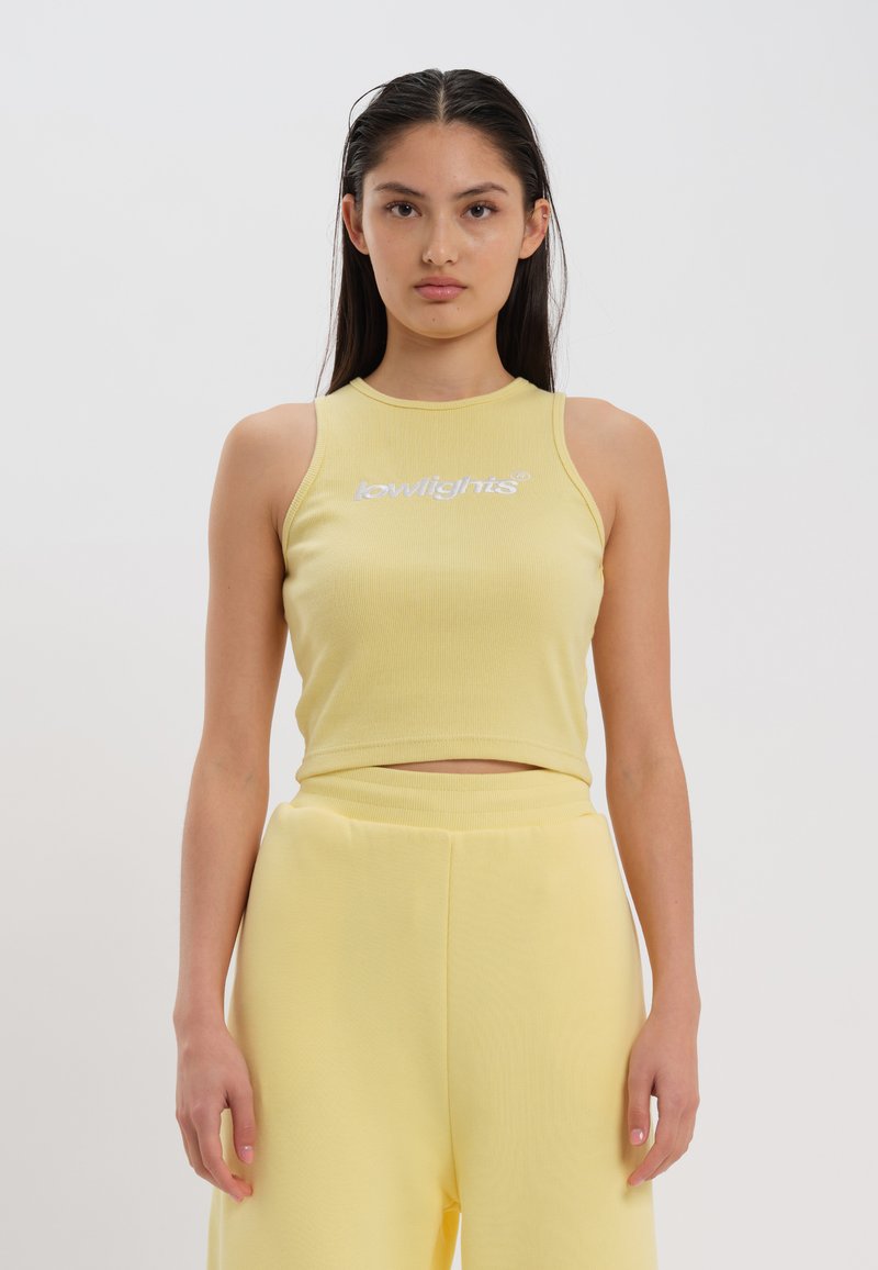 Yellow ribbed crop top with white "lowlights" text, featuring a high neckline and sleeveless design, paired with matching yellow wide-leg pants.