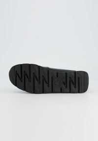 Black athletic shoe sole featuring a textured zigzag pattern and prominent logo, designed for grip and durability.